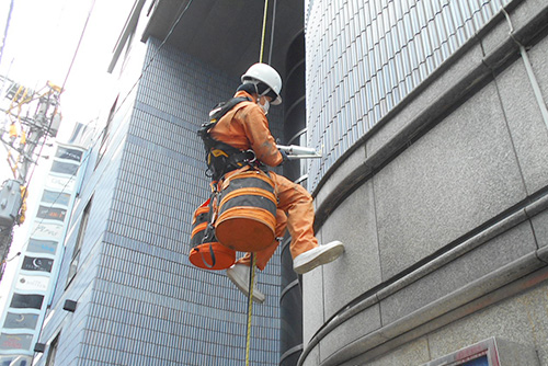 ロープアクセスでアンカーピンニング工法により外壁の補修作業を行う作業員の写真